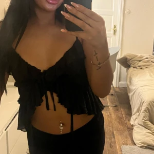 Svart volangtopp - Snygg svart linnetopp med volangdetaljer och knyt framtill. Perfekt för en kväll ute eller en avslappnad dag. Toppen är ärmlös och har en luftig passform.