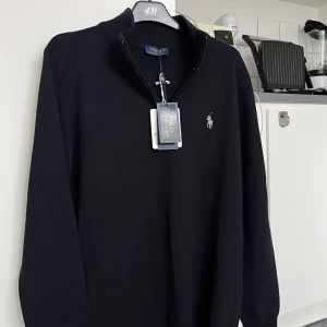 Svart tröja från Polo Ralph Lauren - Snygg mörkblå tröja från Polo Ralph Lauren. Tröjan har en dragkedja vid halsen. Perfekt för en stilren look.