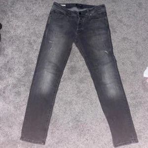 Grå jeans från Jack & Jones - Snygga grå jeans från Jack & Jones med en slim passform. De har en klassisk femficksdesign och en diskret slitning för en trendig look. Perfekta för en avslappnad stil. Tar emot byte 