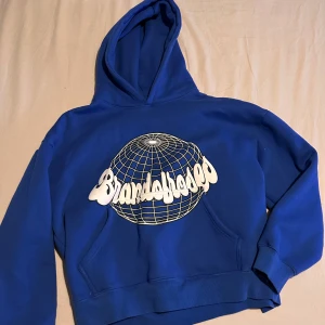 Blå hoodie från Brand of Roses - Säljer en blå hoodie från Brand of Roses med en cool vit grafisk design på framsidan. Perfekt för en avslappnad stil. Den har en klassisk känguruficka och en bekväm huva.