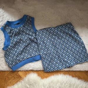 Blå ärmlös topp och kjol från Gina Tricot - Snygg blå ärmlös topp och kjol från Gina Tricot med ett unikt mönster i vitt och mörkblå. Toppen har ribbade kanter vid hals och ärmhål, vilket ger en stilren look. Perfekt för att piffa upp garderoben!