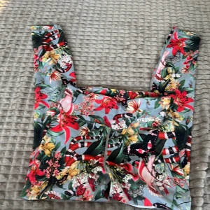 Färgglada blommiga leggings från Stronger - Snygga och färgglada leggings från Stronger med ett blommigt mönster i rött, gult och grönt på en ljus bakgrund. Perfekta för att liva upp träningsgarderoben. De har en bekväm passform och är idealiska för träning.