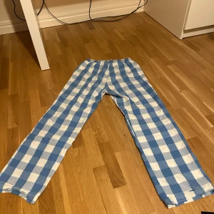 Blåvitrutiga byxor med snörning - Snygga blåvitrutiga byxor med elastisk midja och snörning för extra komfort. Perfekta för en avslappnad stil. Tillverkade i ett mjukt material som känns skönt mot huden.