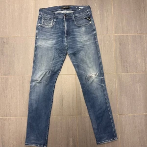Blå jeans från Replay - Snygga blå jeans från Replay med en lätt slitning på ena benet. De har en klassisk femficksdesign och en knappgylf. Perfekta för en avslappnad stil.