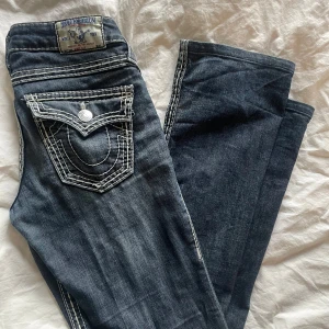 True Religion jeans mörkblå  - Snygga mörkblå jeans från True Religion med vita sömmar och slitna detaljer. De är i jättebra skick förutom att gylfen lossnat lite (se bild 4) men funkar fortfarande som vanligt 🥰🥰 säljer för att de är för små för mig🩷37 cm i midjan rakt över och 79 cm i innerbenslängd❤️❤️