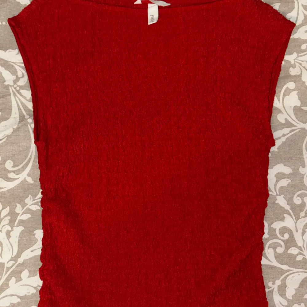Säljer en snygg röd topp från H&M. Den har en texturerad yta och är ärmlös, vilket gör den perfekt för varmare dagar. Toppen har en enkel och stilren design som passar till många olika outfits.. Yläosat.