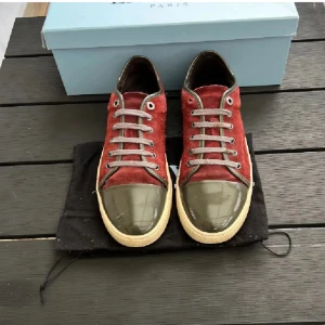 Röda sneakers från Lanvin - Snygga röda sneakers från Lanvin med en unik design. Skorna har en glansig grön tåhätta och snörning framtill. Perfekta för att ge din outfit en stilfull touch.