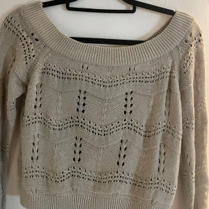 Beige stickad tröja från Only - Säljer en beige stickad tröja från Only med ett vackert hålmönster. Tröjan har en bred ribbad kant vid halsen och långa ärmar. Perfekt för en stilren och mysig look.