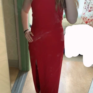 Röd långklänning med slits - Snygg röd långklänning med slits och öppen rygg. Klänningen har smala axelband som korsas i ryggen för en elegant look. Perfekt för festliga tillfällen.