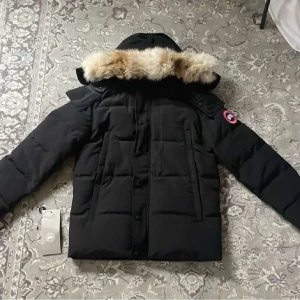 Canada goose  - Säljer en svart dunjacka från Canada Goose med en lyxig pälsdetalj på huvan. Jackan har långa ärmar och en stilren design med knappar och dragkedja framtill. Perfekt för kalla vinterdagar.