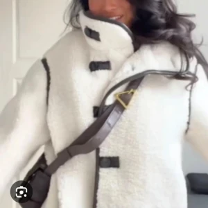 Ny Vit teddyjacka med svarta detaljer  - Säljer en stilren helt ny vit teddyjacka med svarta detaljer och knäppning framtill. Jackan har en hög krage och långa ärmar, perfekt för kyliga dagar. Den är både trendig och bekväm, ett måste i garderoben! Ny med lappen kvar.