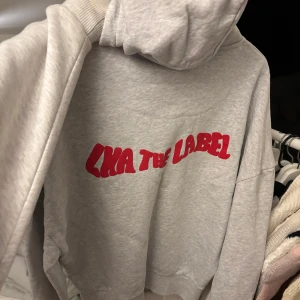 Grå hoodie från LXA The Label - Säljer en grå hoodie från LXA The Label med röd text på ryggen. Den har en klassisk design med huva.  snygg och skön 🩷knappt använd så i fint skick!!!