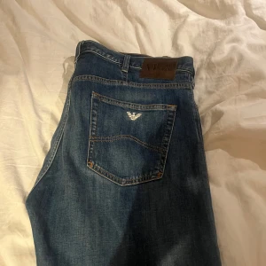 Blå jeans från Armani - Snygga blå jeans från Armani med klassisk femficksdesign och logga på bakfickan. Perfekta för en stilren look. De har en knappgylf och är tillverkade i ett slitstarkt denimtyg.