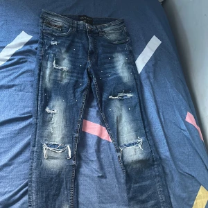 Blå jeans från Supply & Demand - Snygga blå jeans från Supply & Demand med slitna detaljer och en cool, distressed look. De har en normal passform och är perfekta för en avslappnad stil. Midjan är w30 och de har en klassisk femficksdesign.