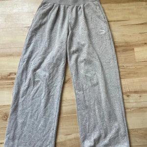 Grå mjukisbyxor från Puma - Säljer ett par grå mjukisbyxor från Puma. Byxorna har en bred resår i midjan och ett broderat Puma-logotyp på sidan. De är tillverkade i mjukt material och har en loose passform för extra komfort.