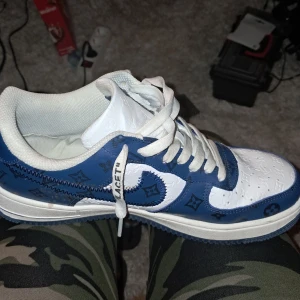 Size 8.5 - Nike Air Force 1 Low by Virgil Abloh x Louis Vuitton LV Blue - Snygga blå och vita sneakers med monogrammönster. Skorna har snörning och en klassisk siluett. Tillverkade i Italien med en stilren design som kombinerar olika texturer och färger.