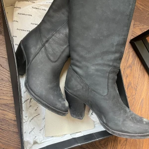 Svarta stövlar med klack - Snygga svarta stövlar i skinn med klack. De har en stilren design och når upp till knäna, vilket gör dem perfekta för både vardag och speciella tillfällen. Enkla att matcha med olika outfits. Går att läder behandla om man vill rusta upp de. Kommer i låda och inlägg till skorna. 