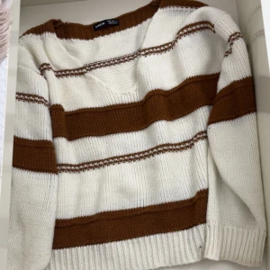 Randig stickad tröja från Shein - Säljer en mysig stickad tröja från Shein i vitt och brunt. Tröjan har ett randigt mönster och en v-ringad hals. Perfekt för kyligare dagar!