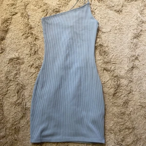 Ljusblå ribbad klänning från H&M Divided - Snygg ljusblå klänning från H&M Divided med en one-shoulder design och ribbad textur. Perfekt för en stilren look. Klänningen har en tight passform som framhäver figuren.