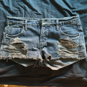 Blå jeansshorts med slitningar - Säljer ett par blå jeansshorts med coola slitningar och fransar. De är lågmidjade. Säljer så de är för stora. De är som nya! Midjemått: 39cm. Säljer för 500 då det är från USA, Pris kan diskuteras! 