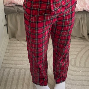 Röda rutiga byxor från XNDX - Säljer ett par bekväma röda byxor med rutig design från XNDX. Byxorna är tillverkade i en återvunnen bomullsblandning och har en avslappnad passform. Perfekta för en mysig dag hemma.