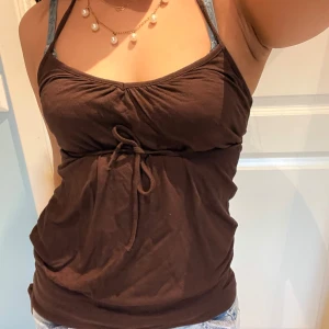 Brunt linne - Brunt linne med anpassbara axelband som syns i bild 2. Banden kan knytas på massa olika sätt, i första bilden är de främre knutna till en halterneck och de bakre till en rosett. Sista bilden visar en knytdetaljen på botten. Toppen är lös med ett tajt parti längst ner! Passar nog XS-M