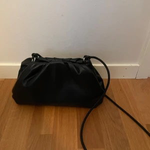 Svart axelremsväska  - Snygg svart axelremsväska köpt på Åhléns. Magnet upptill, och ett smalt band man kan reglera längden på. Väskan är nästan helt ny, då jag köpte den för en månad sen och använt den fåtal gånger, nypris 500. Mått: Längd: 33 cm Djup: 11 cm Höjd: 16 cm