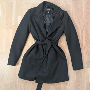 Svart kappa med bälte - Snygg svart kappa från vero Moda med knytbälte i midjan. Den har en klassisk krage och långa ärmar. Perfekt för kyligare dagar med sitt stilrena och tidlösa utseende.💕