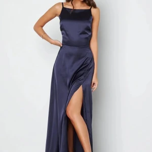Marinblå balklänning  - Suoerfin marinblå balklänning i satin med slits och öppen rygg. Klänningen har spetsdetaljer och smala axelband, perfekt för bal eller bröllop. 