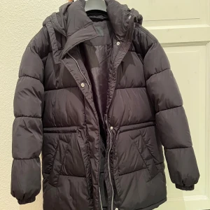 Svart pufferjacka från BikBok - Nästan helt oanvänd. Säljer en svart pufferjacka från BikBok i storlek XS. Jackan har en dragkedja och knappar framtill samt en mysig huva. Perfekt för kyliga dagar med sin vadderade design.