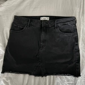Svart jeanskjol - Snygg svart jeanskjol från Mango i storlek M. Kjolen har en klassisk femficksdesign och en rå kant nertill för en cool look. Perfekt för att matcha med olika toppar och accessoarer.