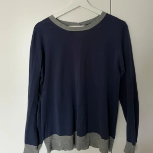 Blå kofta från Filippa K - Snygg blå kofta från Filippa K med gråa detaljer vid krage, ärmslut och nederkant. Koftan har knappar längs ryggen och är tillverkad i 100% bomull. Perfekt för en stilren look. Nypris 1500 kr. 