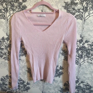 Ljusrosa ribbad tröja från Amisu - Säljer en ljusrosa ribbad tröja från Amisu med v-ringning. Tröjan har långa ärmar och är perfekt för en stilren look. 