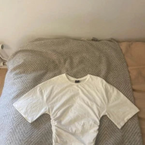 Gina tricot  - Vit t-shirt  men större ärmar från Gina Tricot i storlek XS. Modellen har korta ärmar, rund halsringning och snygga rynkade detaljer i sidorna som ger en cool twist. Tillverkad i mjuk bomull, perfekt för en clean och fräsch look. 