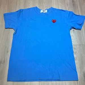 Blå Comme des Garçons Play t-shirt - Snygg blå t-shirt från Comme des Garçons Play i storlek large. Perfekt för dig som gillar stilrena streetwear-plagg! Hör av dig om du har någon fråga eller vill ha fler bilder!