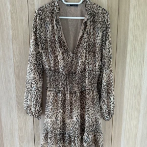 Leopardmönstrad kortklänning från Zara - Snygg kortklänning från Zara med leopardmönster i beige och bruna toner. Klänningen har v-ringning, smockad midja och trekvartsärmar. Lätt och luftig i syntetmaterial, perfekt för dig som vill sticka ut med ett djurmönster. Sömmen har gått sönder i ena armhålan men går lätt att sy ihop!