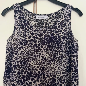 Leopardmönstrad linnetopp XS - Snygg ärmlös linnetopp från Size Needle i XS med svart och vit leopardmönster. Toppen har rund halsringning och är tillverkad i ett lätt och luftigt material, perfekt för att sticka ut med ett coolt mönster.