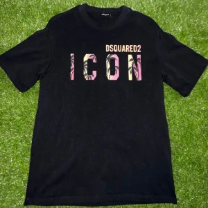 Svart Dsquared2 ICON t-shirt - Svart t-shirt från Dsquared2 med stort tryck 'ICON' i rosa och gult med palmmotiv på bröstet. Klassisk passform och rund hals. Perfekt statement-plagg för dig som gillar streetstyle.