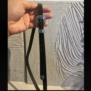  bälte - Snyggt svart bälte i skinnimitation med smal design och croco-mönster. Spännet och detaljerna är silverfärgade.