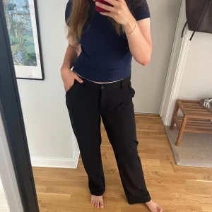 Svarta kostymbyxor från 157, stl M - Svarta kostymbyxor från 157 i rak modell med normal passform. Byxorna har klassisk midja, hällor för bälte och stängs med knapp och dragkedja. Perfekta för en clean och stilren look, passar till allt och är superenkla att styla.