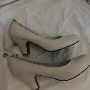 Beige klackskor  från Gyllene Gripen - Stilrena pumps i beige skinn från Gyllene Gripen. Skorna har rund tå, låg klack och en smal rem runt vristen som ger en klassisk look. Perfekta för dig som gillar en enkel men elegant stil. Snygga till både kjol och byxor.( notera liten repa)