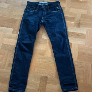Mörkblå Replay jeansbyxor - Säljer ett par mörkblå jeansbyxor från Replay med klassisk femficksdesign och kontrastsömmar. Byxorna har normal passform och raka ben, samt tydlig Replay-logga vid fickan. Midjemått W30 och längd 32.