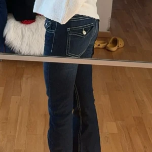 Blå bootcut jeans med vita sömmar - Snygga blå jeans med tydliga vita kontrastsömmar och bootcut-modell. Jeansen har klassiska fickor med lock och knapp bak, samt låg midja. Materialet är jeans och passformen är slim upptill med utsvängda ben. storlek 158 tall o passar mig som bär 32-36 i jeans! jag är 163 för reverens 