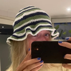 virkad buckethat i grönt, blått & vitt -  virkad bucket hat med bred, vågig brätte. Randigt mönster i grönt, blått och vitt. Mjuk och bekväm passform.
