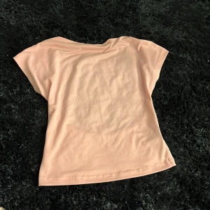 Ljusrosa kortärmad topp - Säljer en ljusrosa topp med korta ärmar och rund hals. Toppen har en enkel och clean design med lätt insvängd midja för en snygg passform. Perfekt att matcha med jeans eller kjol för en fräsch look.