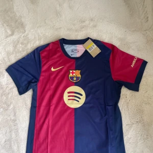 FC Barcelona Nike fotbollströja blå/röd - FC Barcelona matchtröja från Nike med klassisk halvblå och halvröd design. Tröjan har klubbmärke, Nike-logga och sponsorer tryckta i gult. Tillverkad i Dri-FIT-material som andas. Kortärmad modell med rund hals och detaljer på ärmarna.
