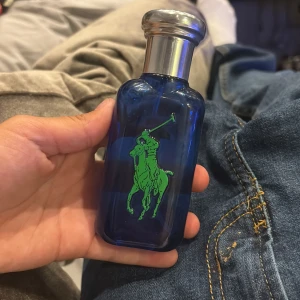 Ralph Lauren Big Pony 1 Blå Parfym - Snygg parfymflaska från Ralph Lauren Big Pony Collection, nummer 1. Flaskan är blå med en stor gul etta på ena sidan och grönt polospel-tryck på andra. Silverfärgad kork i metall-look. Perfekt för dig som gillar sportig och fräsch stil. Finns runt 40/50ml kvar.