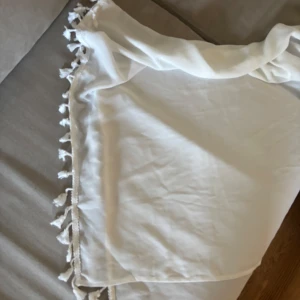 Vit strand sarong  - Säljer en vit strand sarong / kjol med snygga fransar längs kanten. Perfekt att knyta med bikini / baddräkt. 