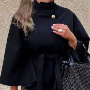 Svart kappa med bälte och knapp - Stilren svart kappa med hög krage, dekorativ guldig knapp vid halsen och knytbälte i midjan. Jackan har vida ärmar och en elegant, minimalistisk look som passar perfekt till höst och vinter.
