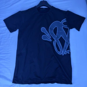  Svart Syna World T-shirt (Pris kan diskuteras) (oanvänd) - (Pris kan diskuteras vid snabba affärer) Svart t-shirt med korta ärmar och stor, grå grafisk print som sträcker sig över både fram- och baksidan. T-shirten har en klassisk rund halsringning och är tillverkad i ett mjukt material som känns skönt mot huden. Perfekt för dig som gillar streetwear och unika tryck.